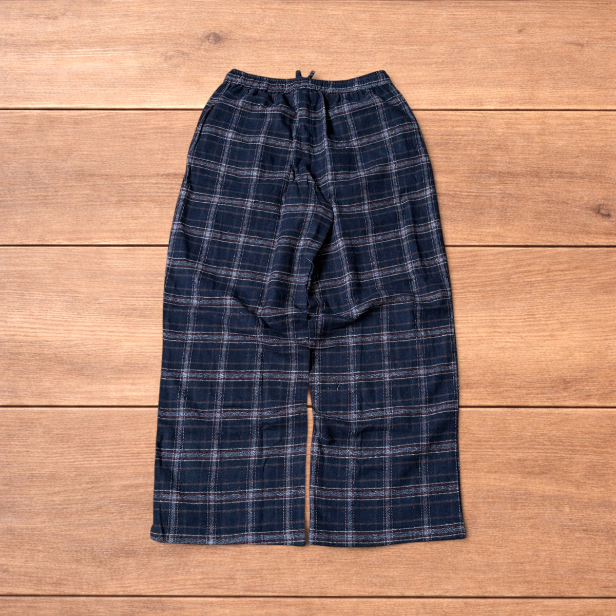 Navy and burgundy plaid baggy loungewear trousers with elasticated waistband and wide legs laid flat on wood surface.