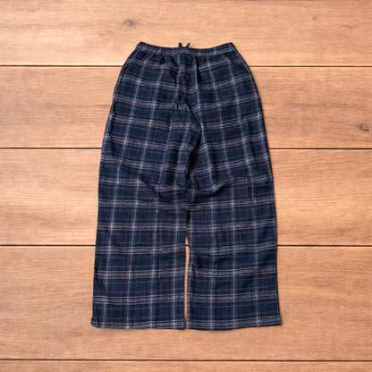 Navy and burgundy plaid baggy loungewear trousers with elasticated waistband and wide legs laid flat on wood surface.
