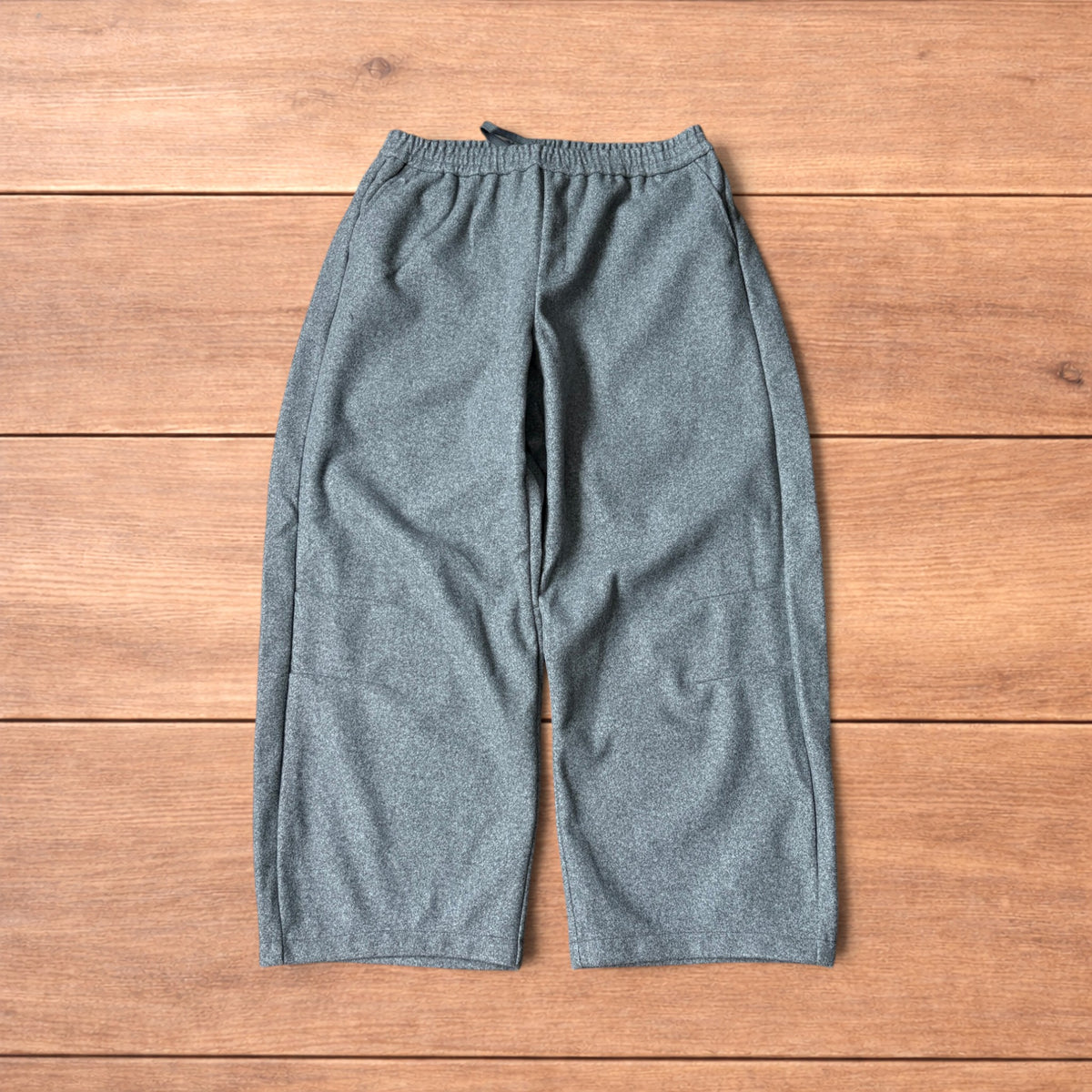 Grey baggy wool trousers with elasticated waist and wide legs laid flat on wooden floor.