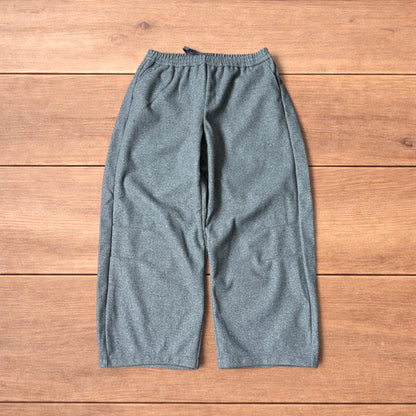 Grey baggy wool trousers with elasticated waist and wide legs laid flat on wooden floor.
