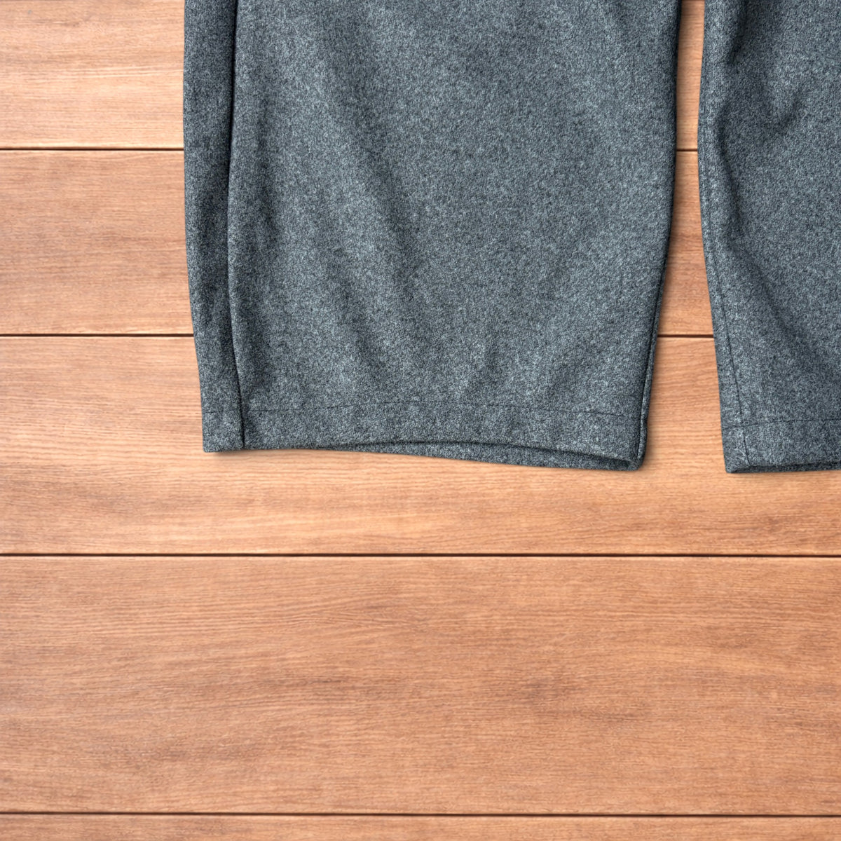 Grey baggy wool trousers with elasticated waist and wide legs laid flat on wooden floor.