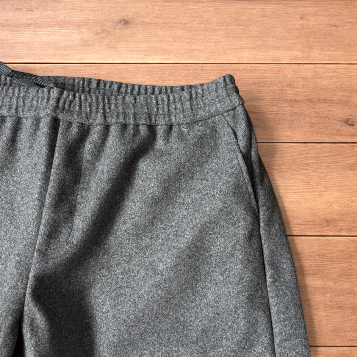 Grey baggy wool trousers with elasticated waist and wide legs laid flat on wooden floor.