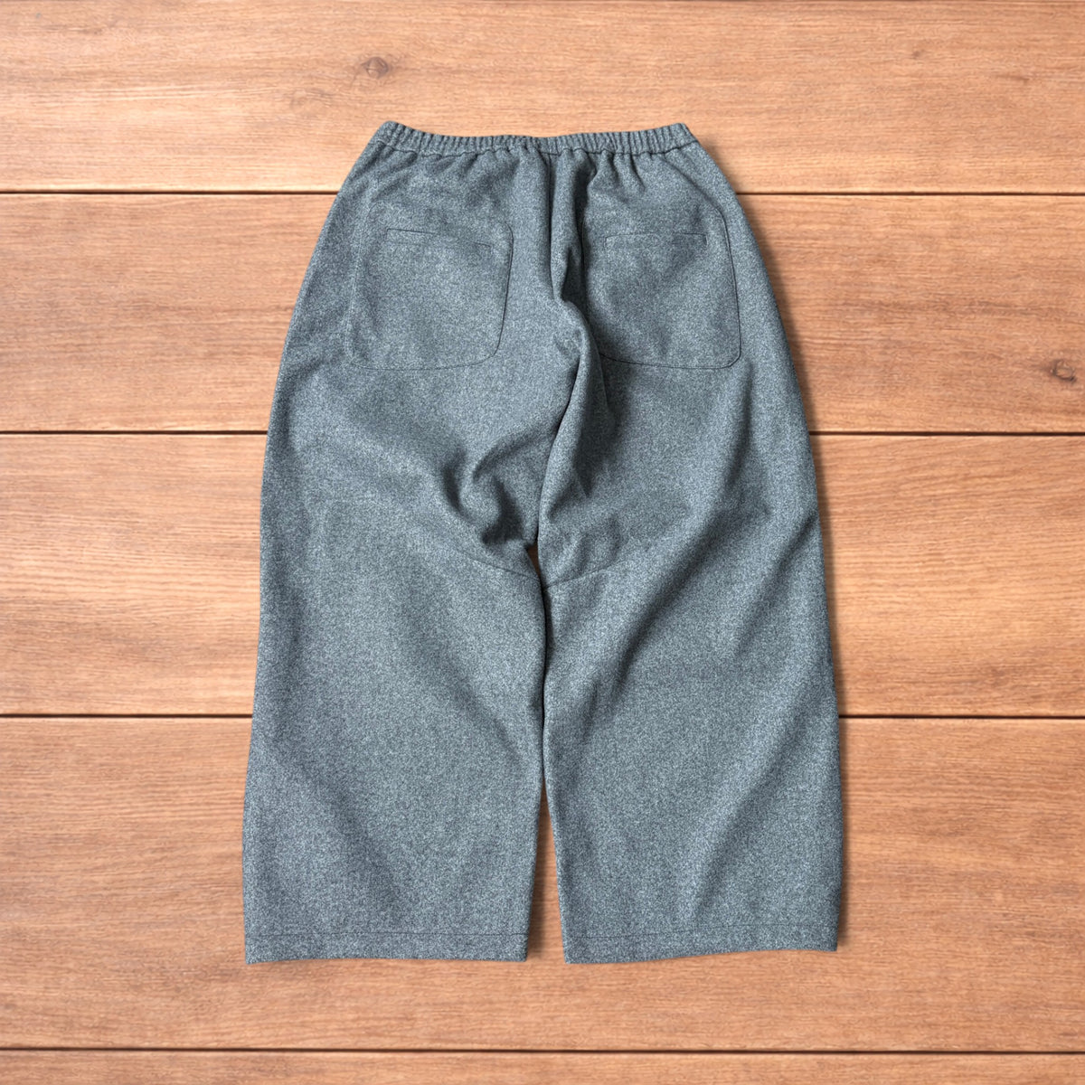 Grey baggy wool trousers with elasticated waist and wide legs laid flat on wooden floor.
