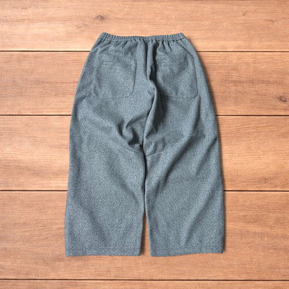 Grey baggy wool trousers with elasticated waist and wide legs laid flat on wooden floor.