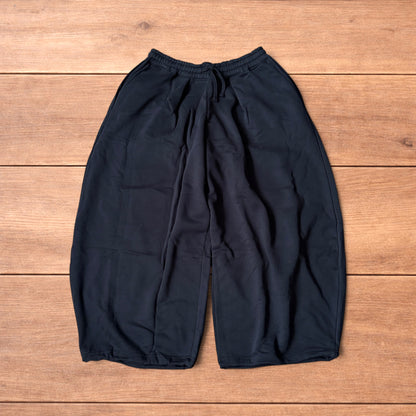 Black baggy joggers laid flat on wooden surface showing elasticated waistband, drawstring and elasticated ankle hems.