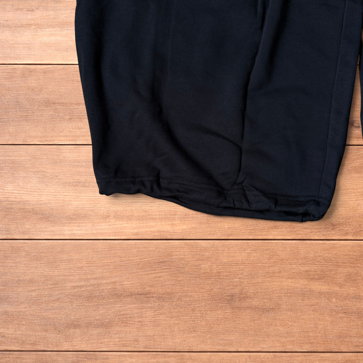 Black baggy joggers laid flat on wooden surface showing elasticated waistband, drawstring and elasticated ankle hems.
