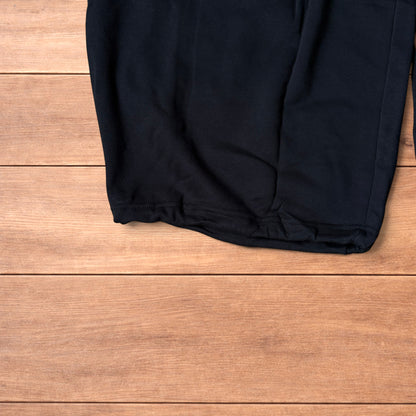Black baggy joggers laid flat on wooden surface showing elasticated waistband, drawstring and elasticated ankle hems.