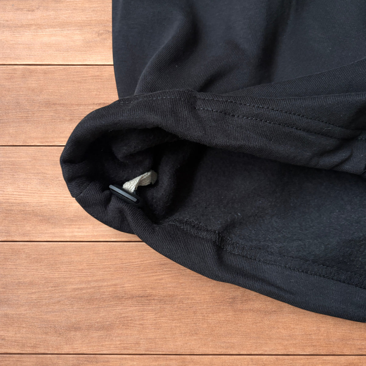 Black baggy joggers laid flat on wooden surface showing elasticated waistband, drawstring and elasticated ankle hems.