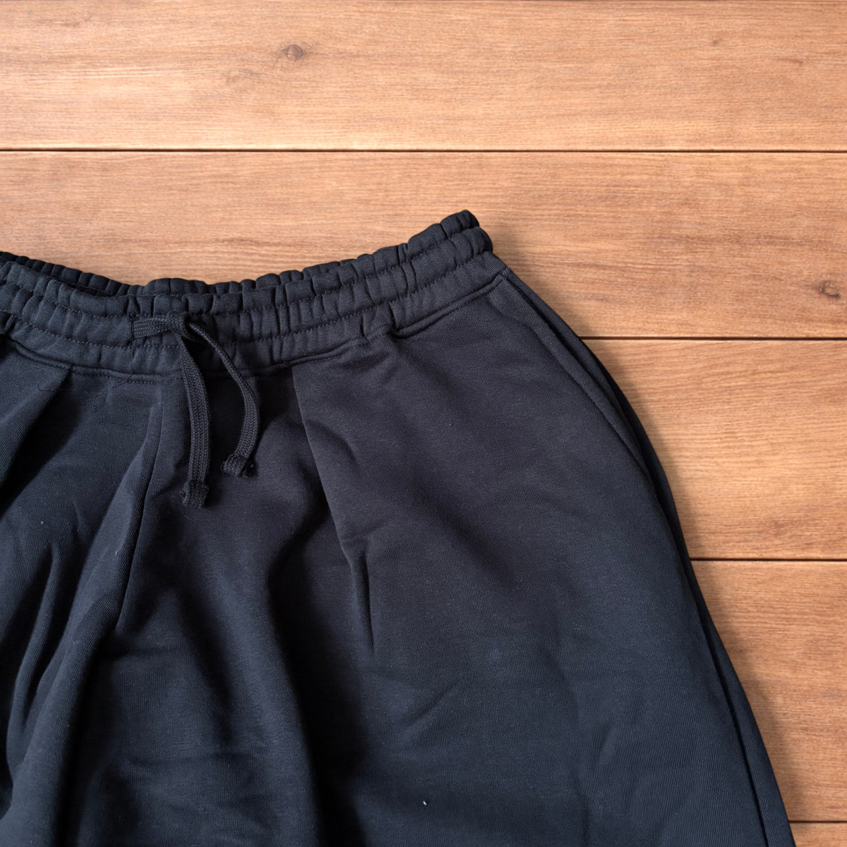 Black baggy joggers laid flat on wooden surface showing elasticated waistband, drawstring and elasticated ankle hems.
