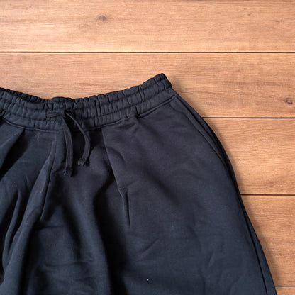 Black baggy joggers laid flat on wooden surface showing elasticated waistband, drawstring and elasticated ankle hems.