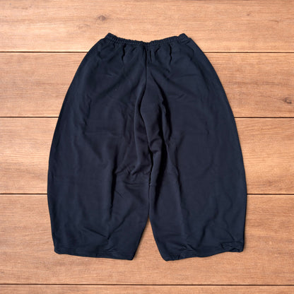 Black baggy joggers laid flat on wooden surface showing elasticated waistband, drawstring and elasticated ankle hems.
