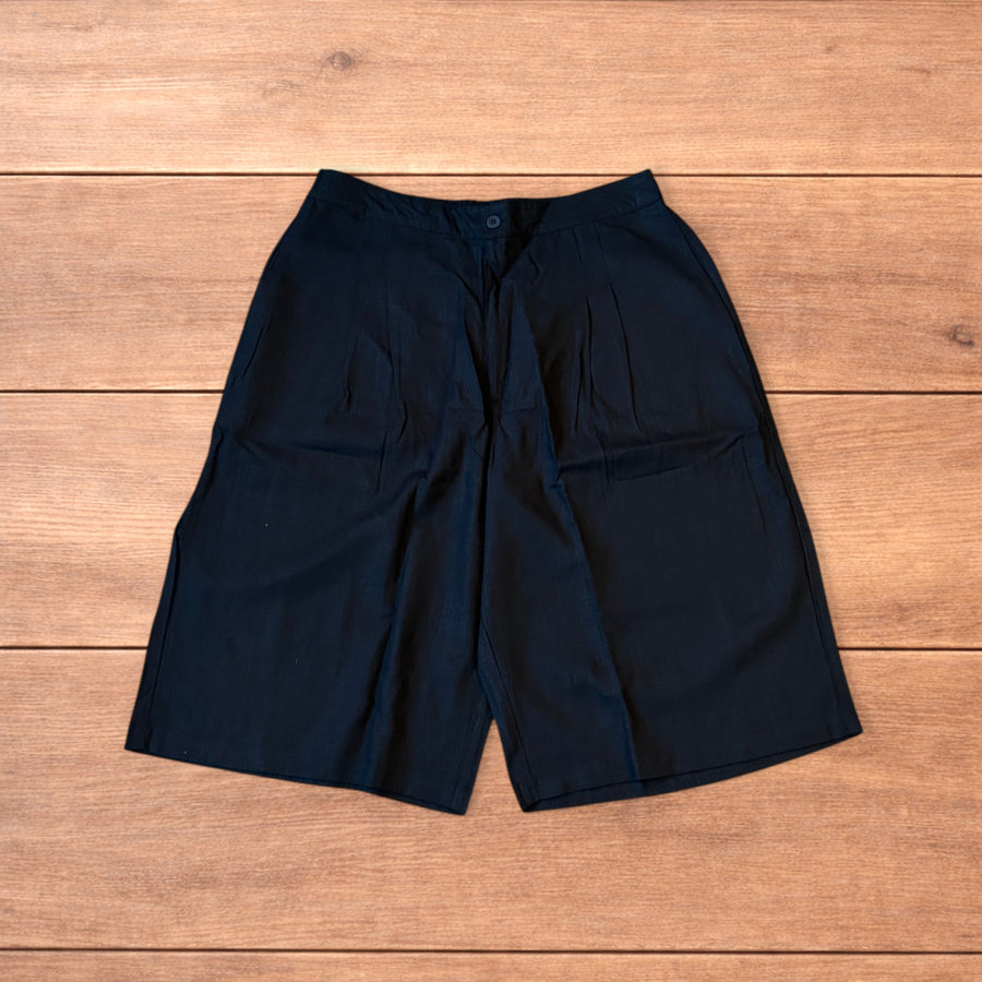Black super baggy wide leg linen shorts jorts laid flat on wooden surface showing front, back, and waistband details.