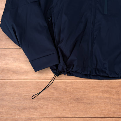 Black outdoor windbreaker jacket with hood, zip pockets and toggled hem laid flat on wooden surface.