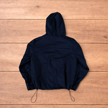 Black outdoor windbreaker jacket with hood, zip pockets and toggled hem laid flat on wooden surface.