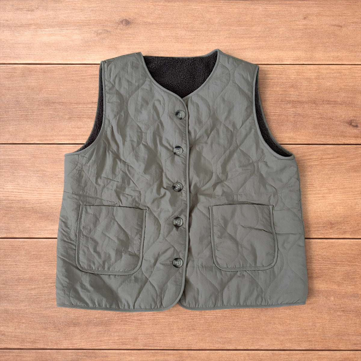 Korean military quilted gilet in khaki with button-up front and fleece inner laid flat on wooden surface.