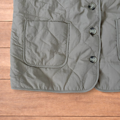 Korean military quilted gilet in khaki with button-up front and fleece inner laid flat on wooden surface.