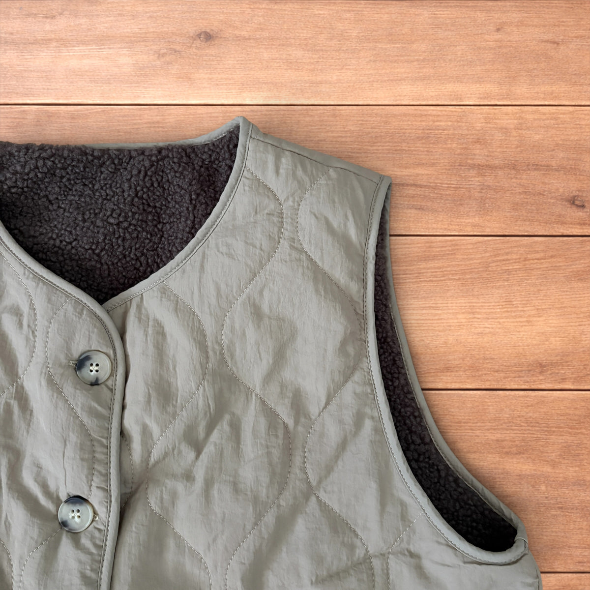 Korean military quilted gilet in khaki with button-up front and fleece inner laid flat on wooden surface.