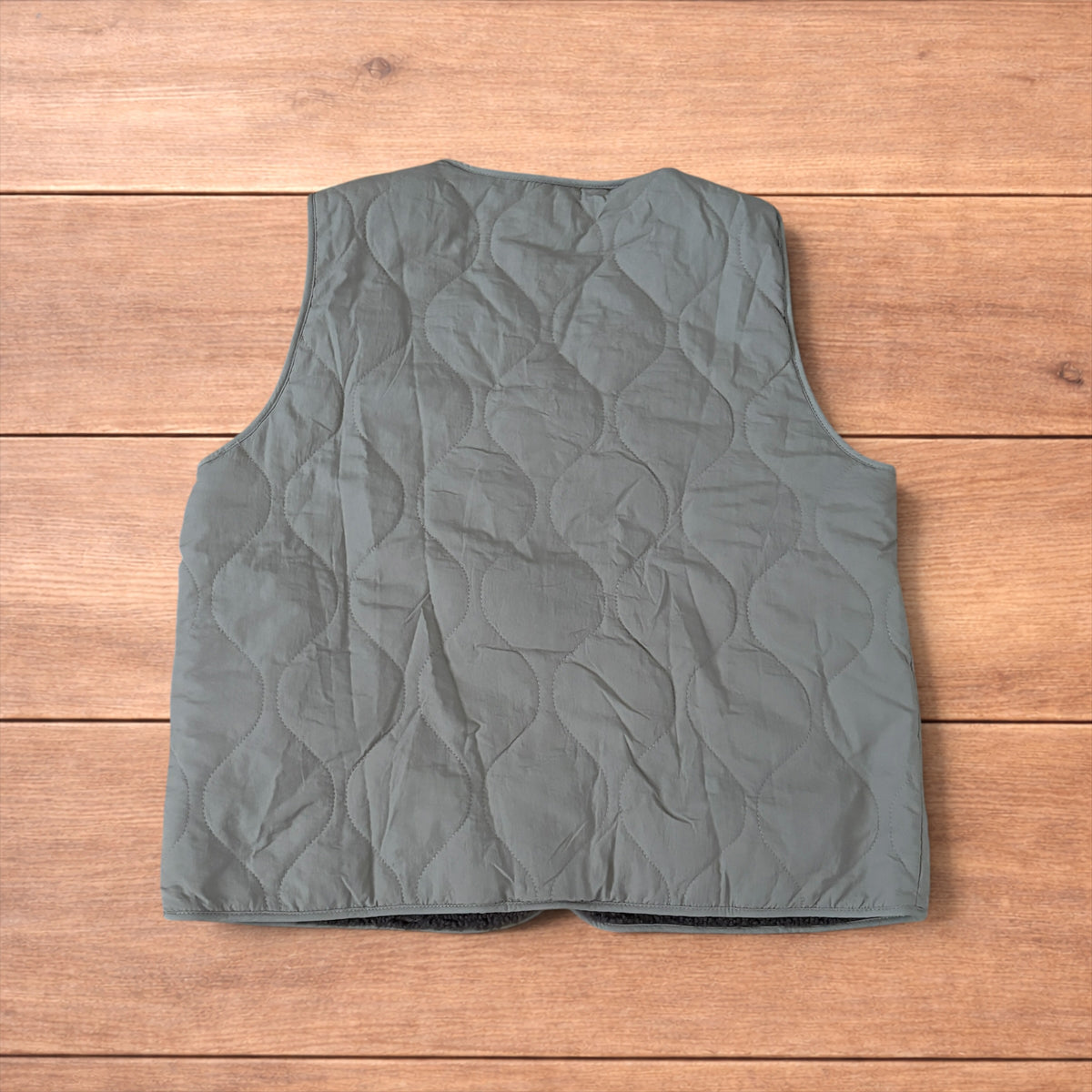 Korean military quilted gilet in khaki with button-up front and fleece inner laid flat on wooden surface.