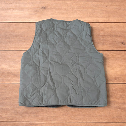 Korean military quilted gilet in khaki with button-up front and fleece inner laid flat on wooden surface.