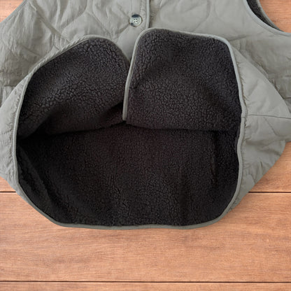 Korean military quilted gilet in khaki with button-up front and fleece inner laid flat on wooden surface.