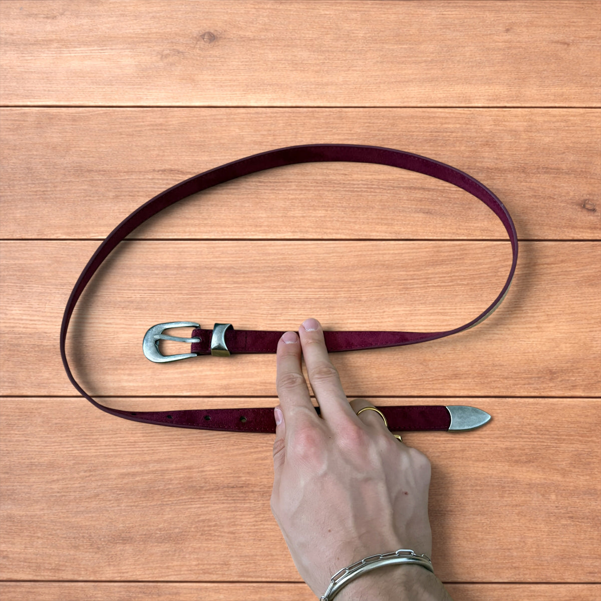 Vintage style red suede cowboy belt with silver buckle and tip on wooden surface.