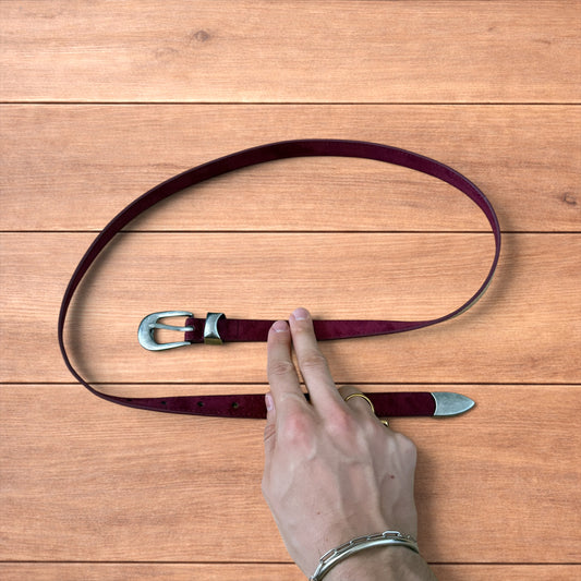 Vintage style red suede cowboy belt with silver buckle and tip on wooden surface.