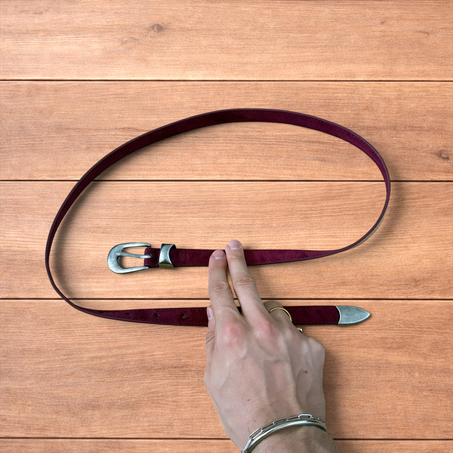 Vintage style red suede cowboy belt with silver buckle and tip on wooden surface.