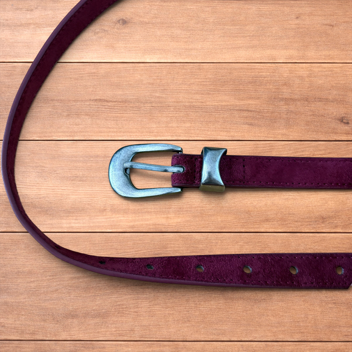Vintage style red suede cowboy belt with silver buckle and tip on wooden surface.