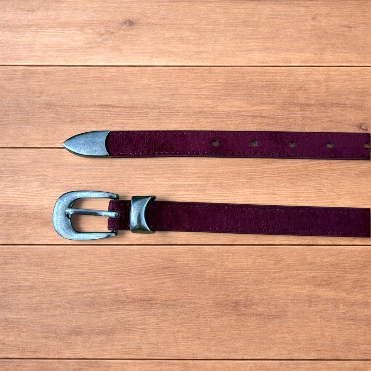 Vintage style red suede cowboy belt with silver buckle and tip on wooden surface.