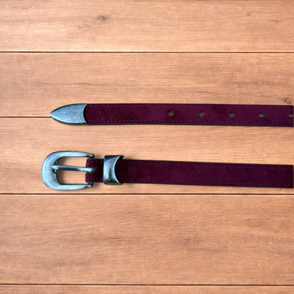 Vintage style red suede cowboy belt with silver buckle and tip on wooden surface.