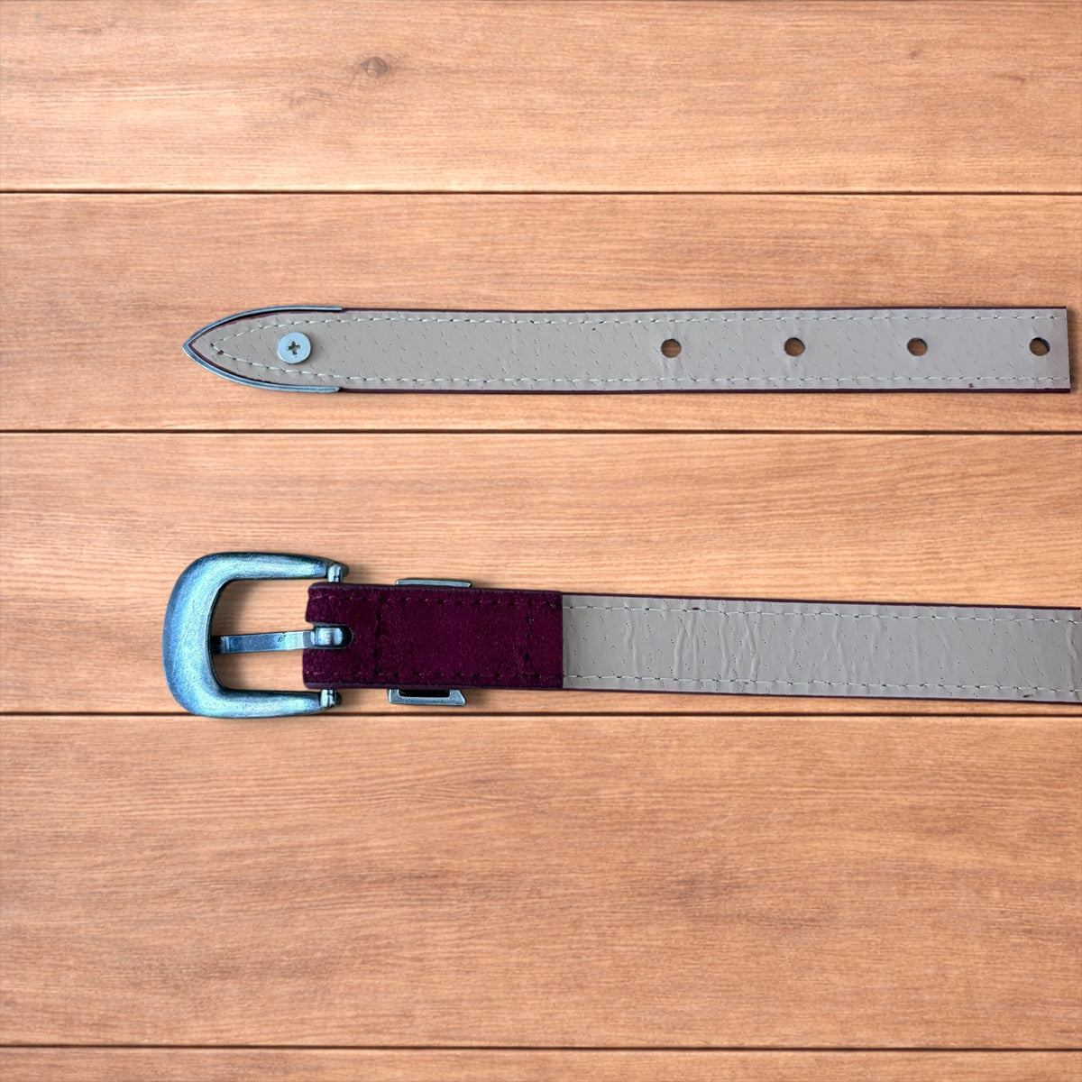 Vintage style red suede cowboy belt with silver buckle and tip on wooden surface.