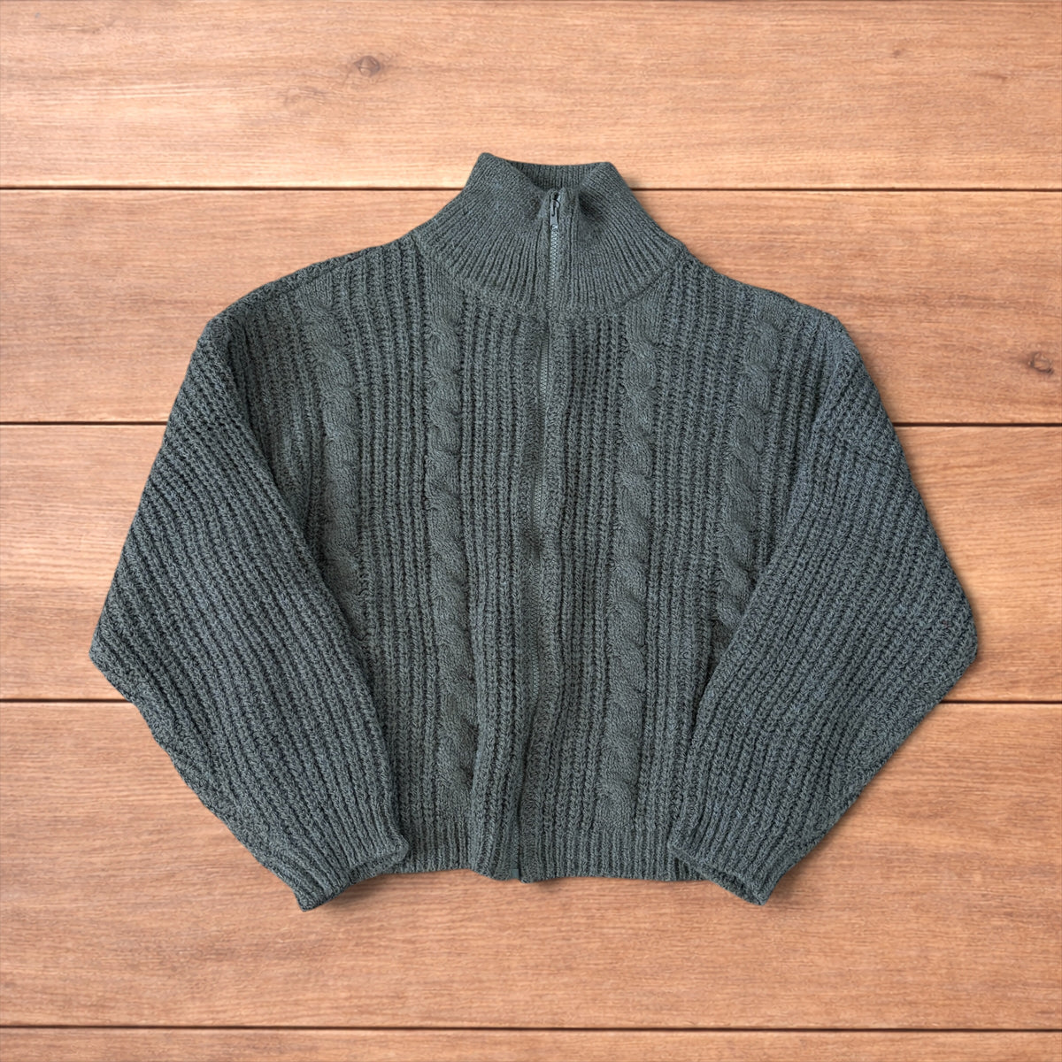 Dark green vintage style knitted cardigan jumper with cable knit pattern and full zip collar laid flat on wooden background.