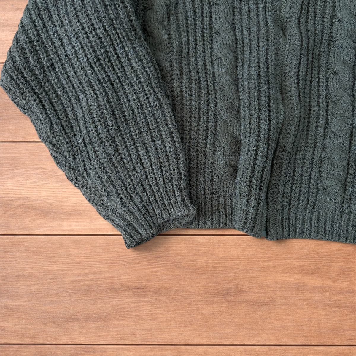 Dark green vintage style knitted cardigan jumper with cable knit pattern and full zip collar laid flat on wooden background.