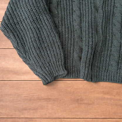Dark green vintage style knitted cardigan jumper with cable knit pattern and full zip collar laid flat on wooden background.