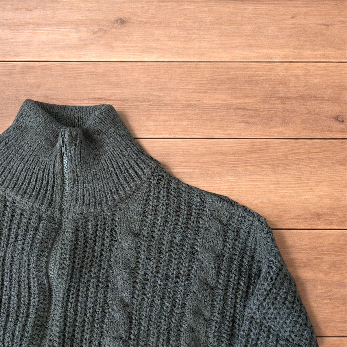 Dark green vintage style knitted cardigan jumper with cable knit pattern and full zip collar laid flat on wooden background.