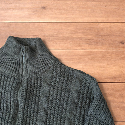 Dark green vintage style knitted cardigan jumper with cable knit pattern and full zip collar laid flat on wooden background.