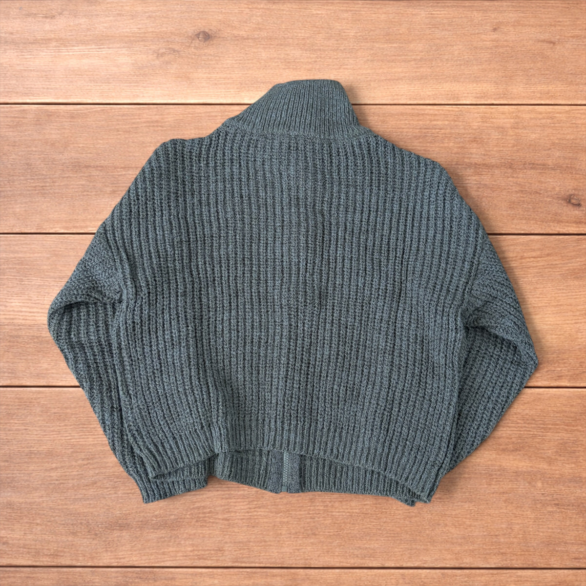 Dark green vintage style knitted cardigan jumper with cable knit pattern and full zip collar laid flat on wooden background.