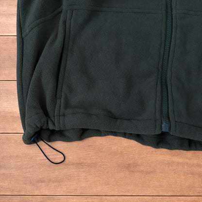 Dark green fleece utility gilet with zip pockets, drawstring neck, and toggled hem laid flat on wooden surface.