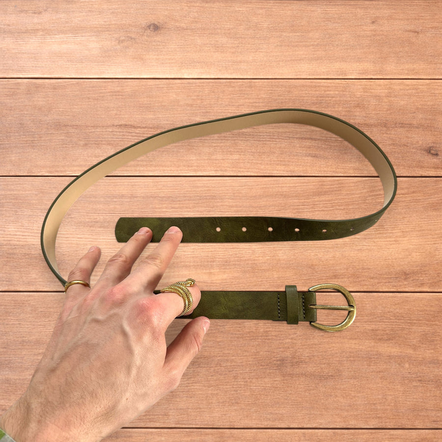 Olive green vintage style faux leather boho cowboy belt with gold metallic buckle laid flat on wood background