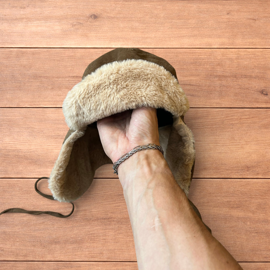 Brown Russian ushanka trapper hat with beige faux fur ear flaps displayed on hand against wooden background