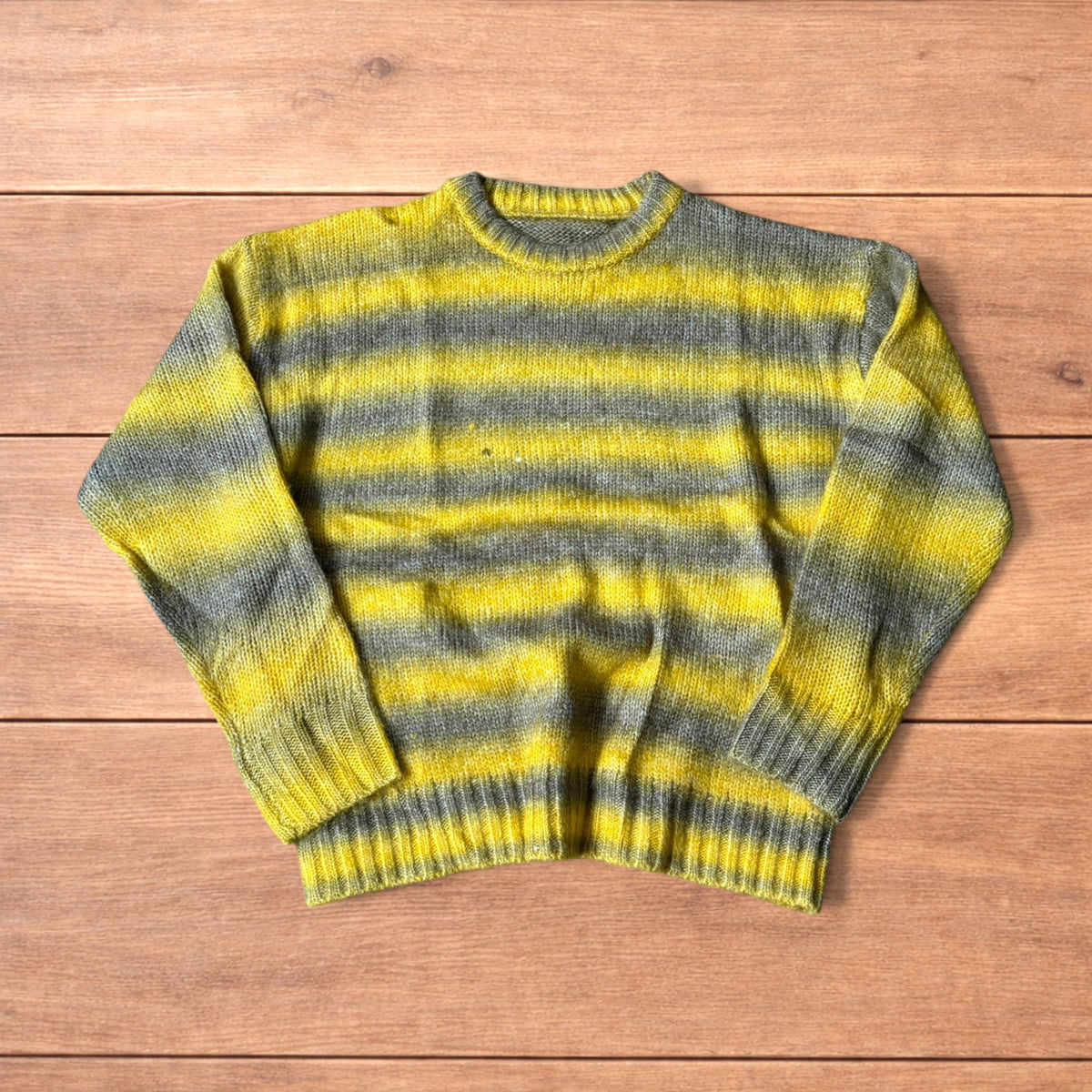 Vintage style baggy knitted sweater jumper with yellow and grey stripes laid flat on wooden surface.