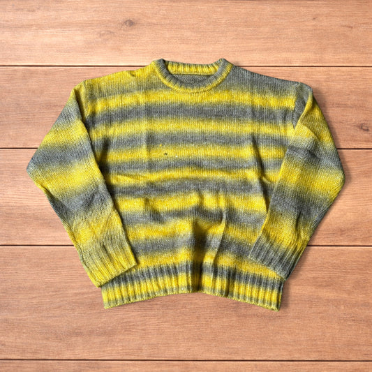 Vintage style baggy knitted sweater jumper with yellow and grey stripes laid flat on wooden surface.