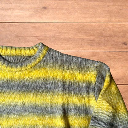Vintage style baggy knitted sweater jumper with yellow and grey stripes laid flat on wooden surface.