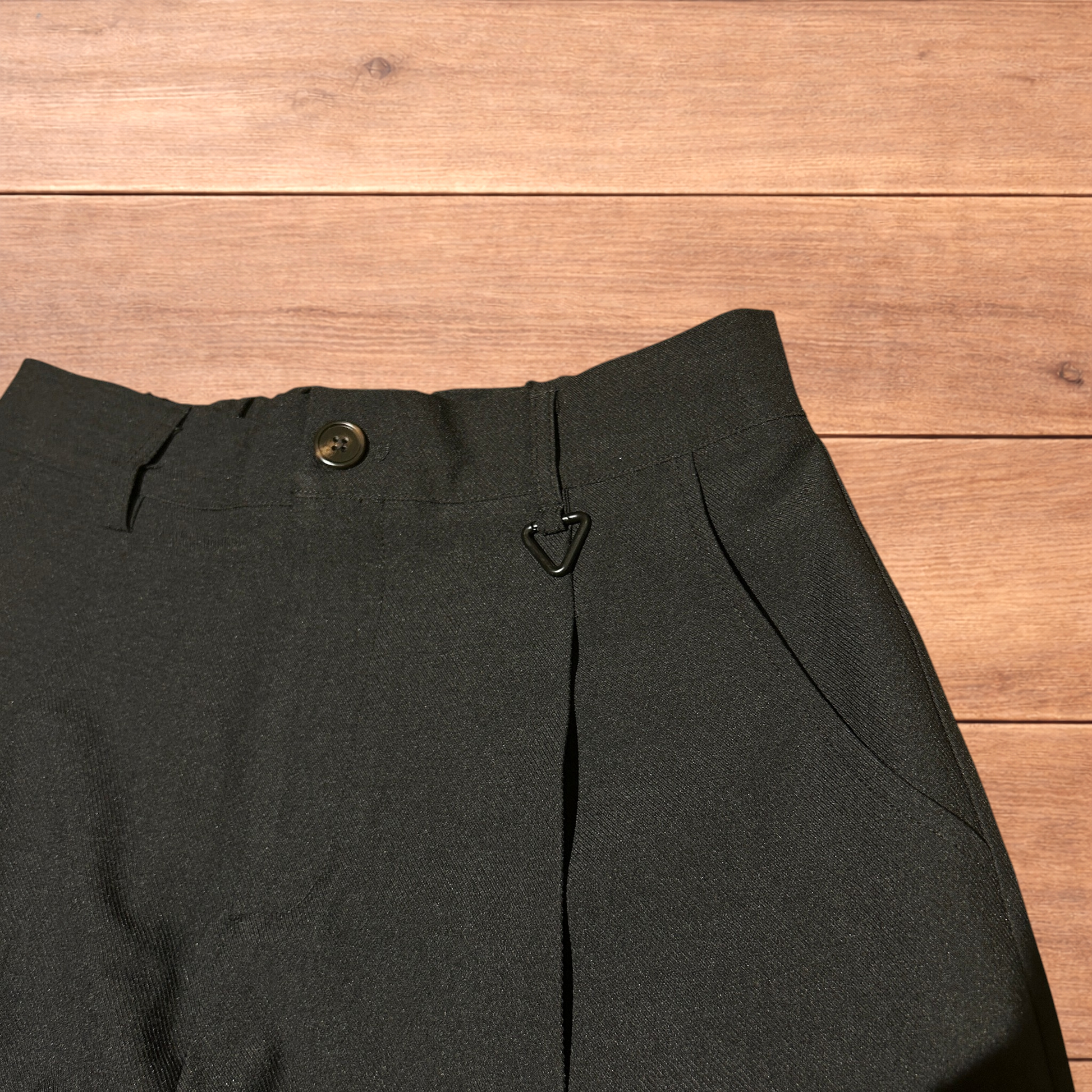 Black baggy wide leg tailored trousers with pleats and white stitch detail, laid flat on wood surface