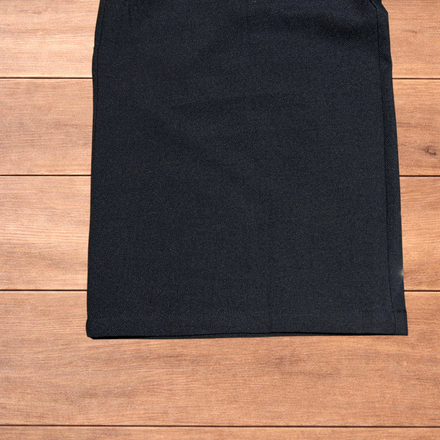 Black baggy wide leg tailored trousers with pleats and white stitch detail, laid flat on wood surface