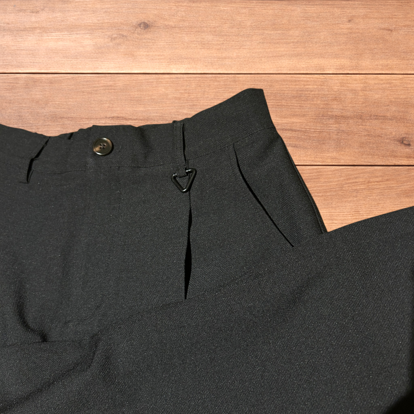 Black baggy wide leg tailored trousers with pleats and white stitch detail, laid flat on wood surface