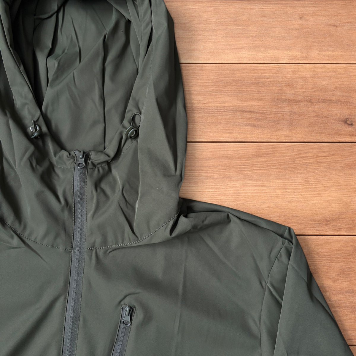 Khaki green lightweight shell anorak jacket with quarter zip and hood laid flat on wood surface.