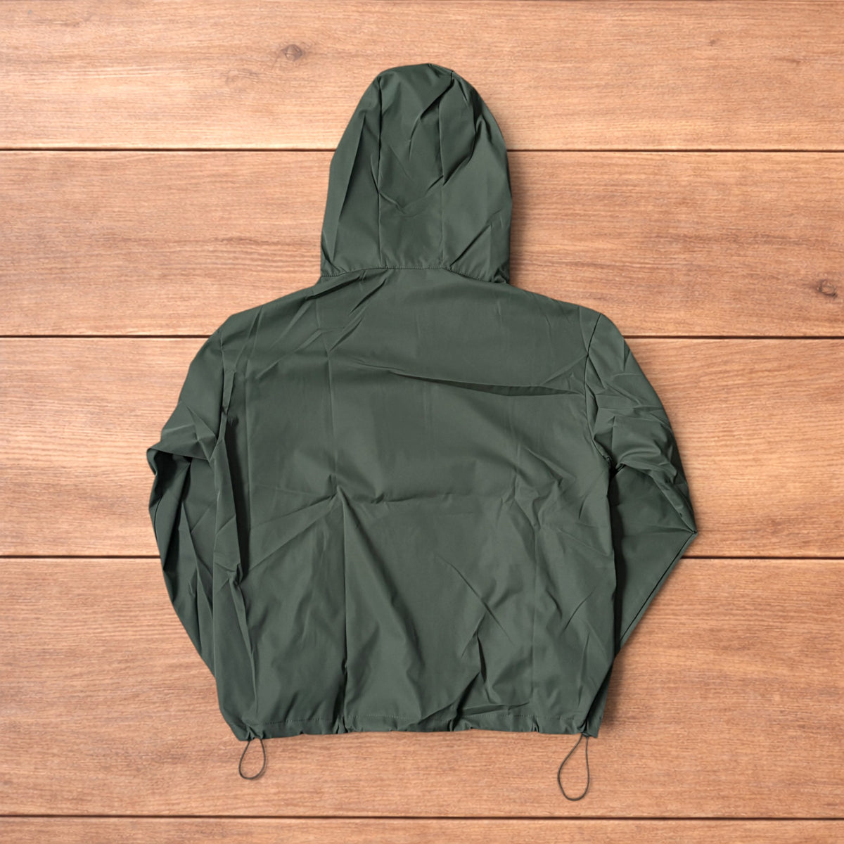 Khaki green lightweight shell anorak jacket with quarter zip and hood laid flat on wood surface.
