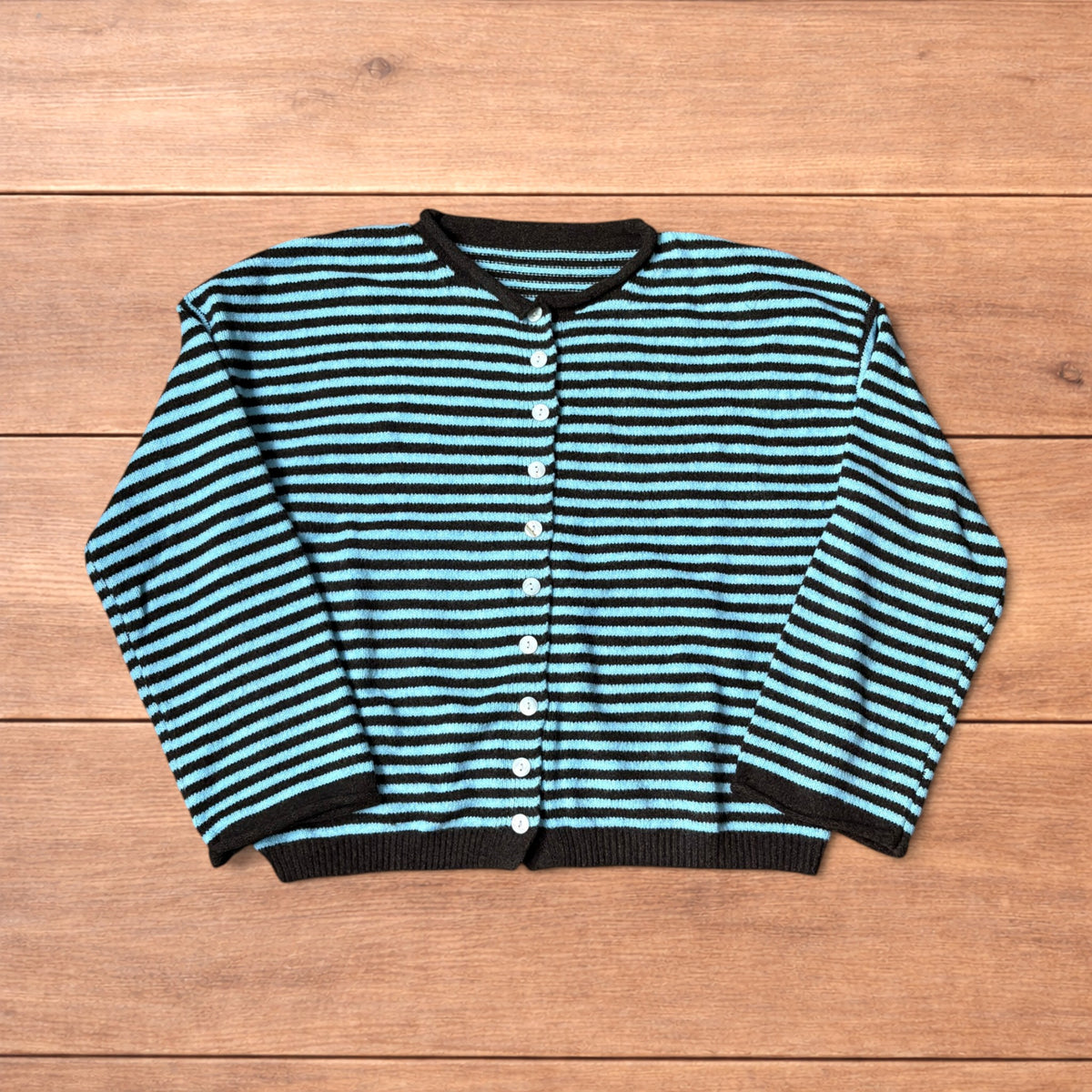 Turquoise and black striped vintage knitted cardigan jumper with button-up front laid flat on wooden surface.