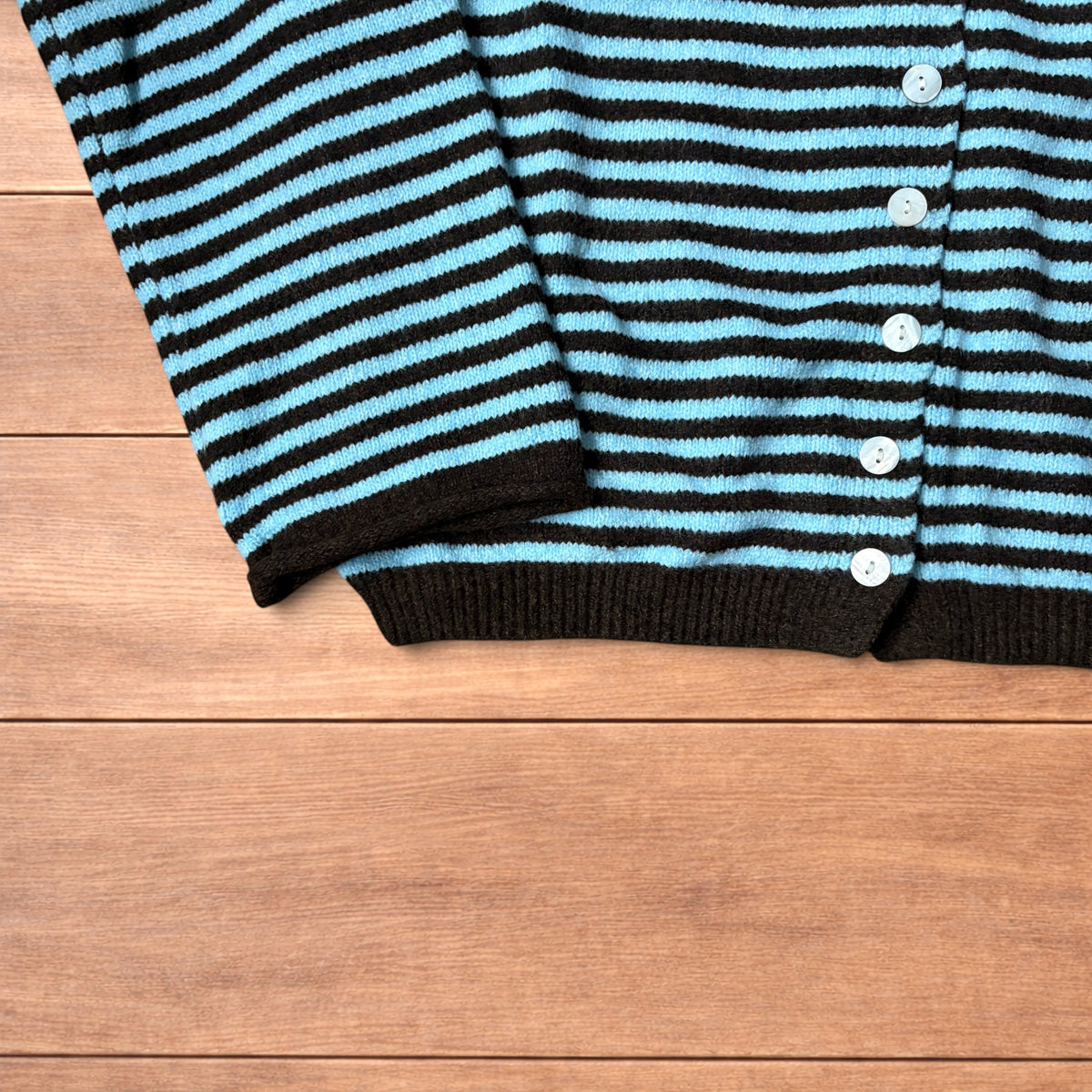 Turquoise and black striped vintage knitted cardigan jumper with button-up front laid flat on wooden surface.